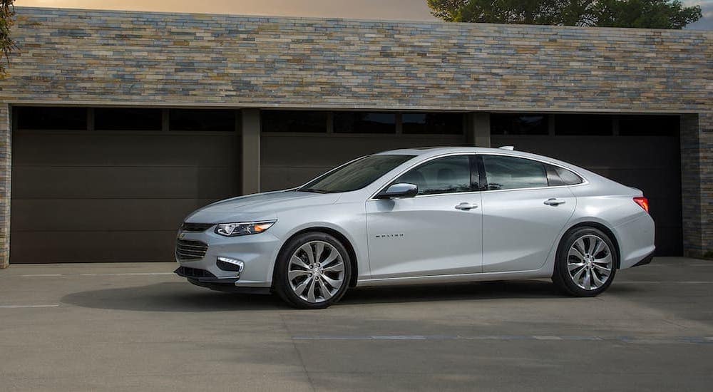 A silver 2017 Chevy Malibu is shown parked outside of a garage.