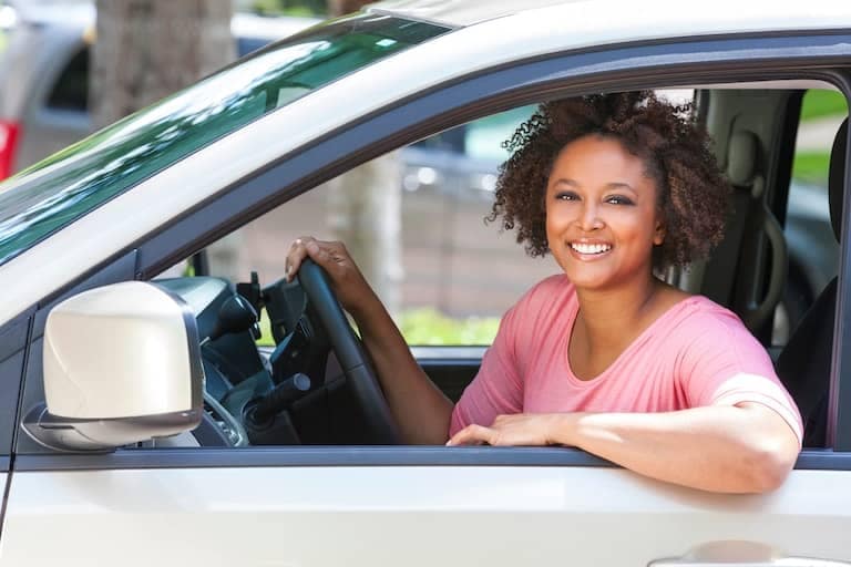 woman smiling with one arm out the driver's side window