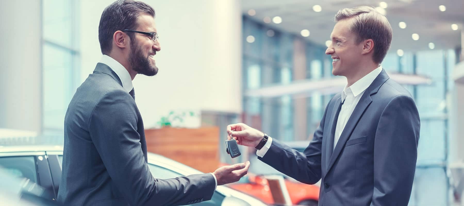 smiling salesman handing car keys to business man