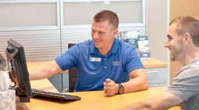 A man sitting inside a dealership, looking at his computer with a customer.