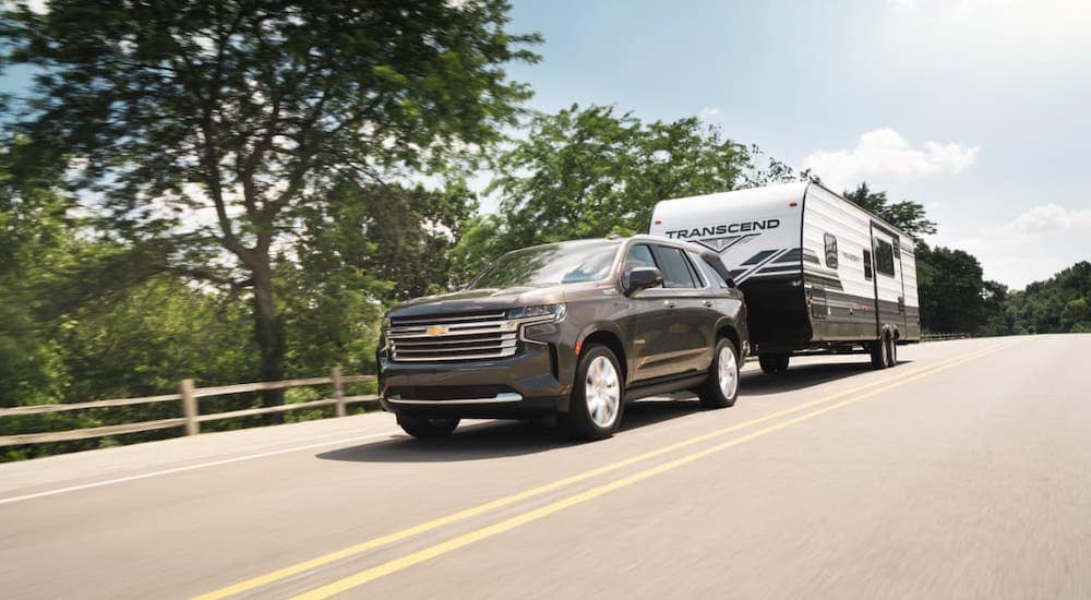 A brown 2021 Chevy Tahoe High Country is towing a trailer on a tree-lined highway.