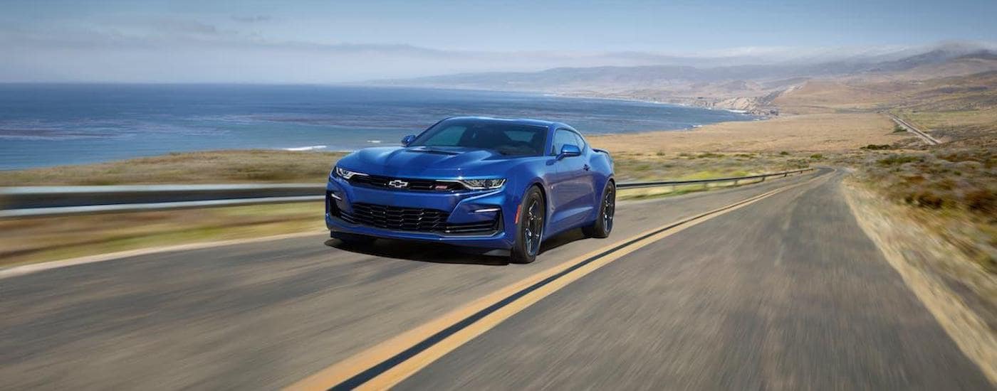 A bright blue 2020 Chevy Camaro SS is driving along a coastal highway.