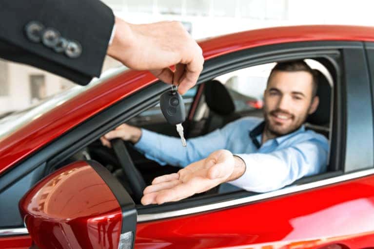 Person being handed a set of car keys while sitting in the drivers seat of a vehicle