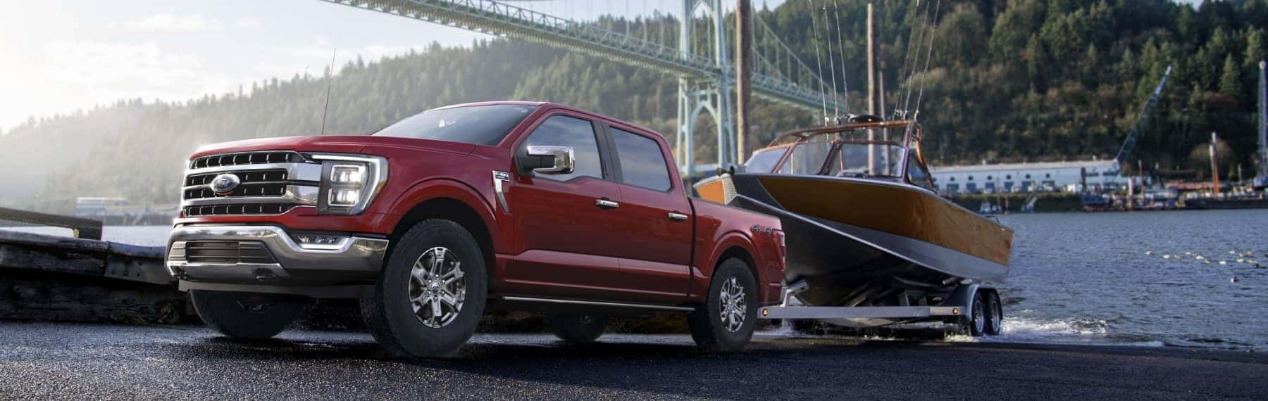 Ford truck pulling a boat out of water with a large suspension bridge in the background. - DeNooyer Ford