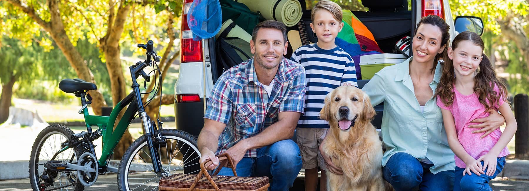 family posing for picture in front of their hatchback full of camping supplies