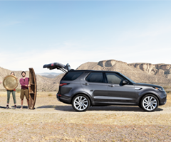 People standing next to their Land Rover with the trunk open in a desert.
