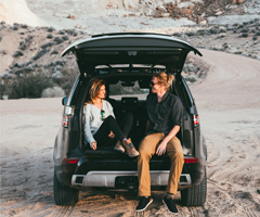 Two people sitting in the trunk of their Land Rover on the beach.