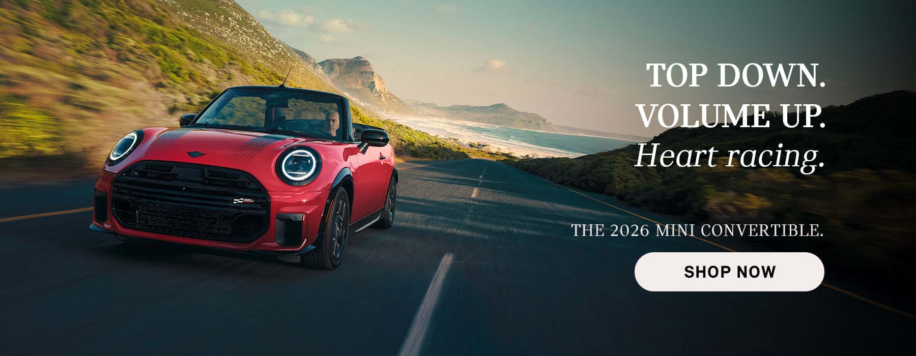 Red MINI convertible driving along a coastal road with mountains and ocean in the background, with advertisement text promoting the 2026 Mini Convertible and a “Shop Now” button.