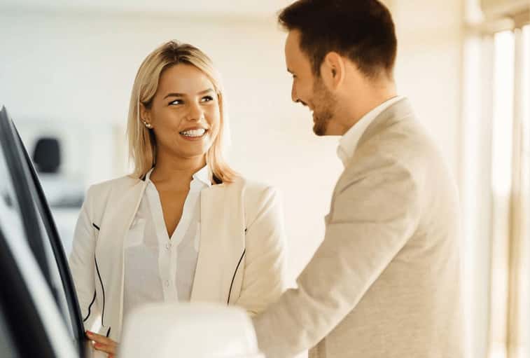 happy woman with car salesman in auto showroom