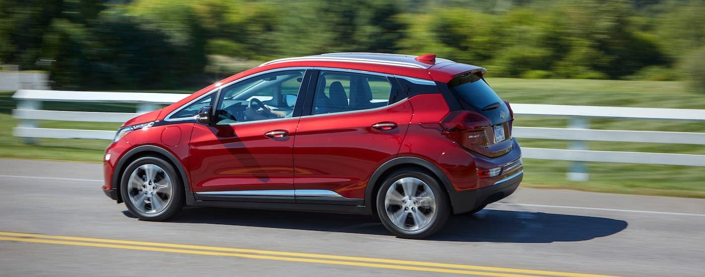 A red 2020 Chevy Bolt EV is driving on a highway near Suffolk, VA, and shown from the side.