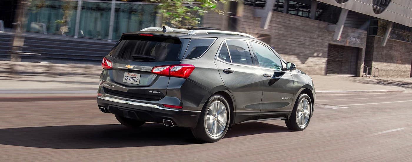 A grey 2020 Chevy Equinox is driving on a city street after leaving a Chevy dealer near me.