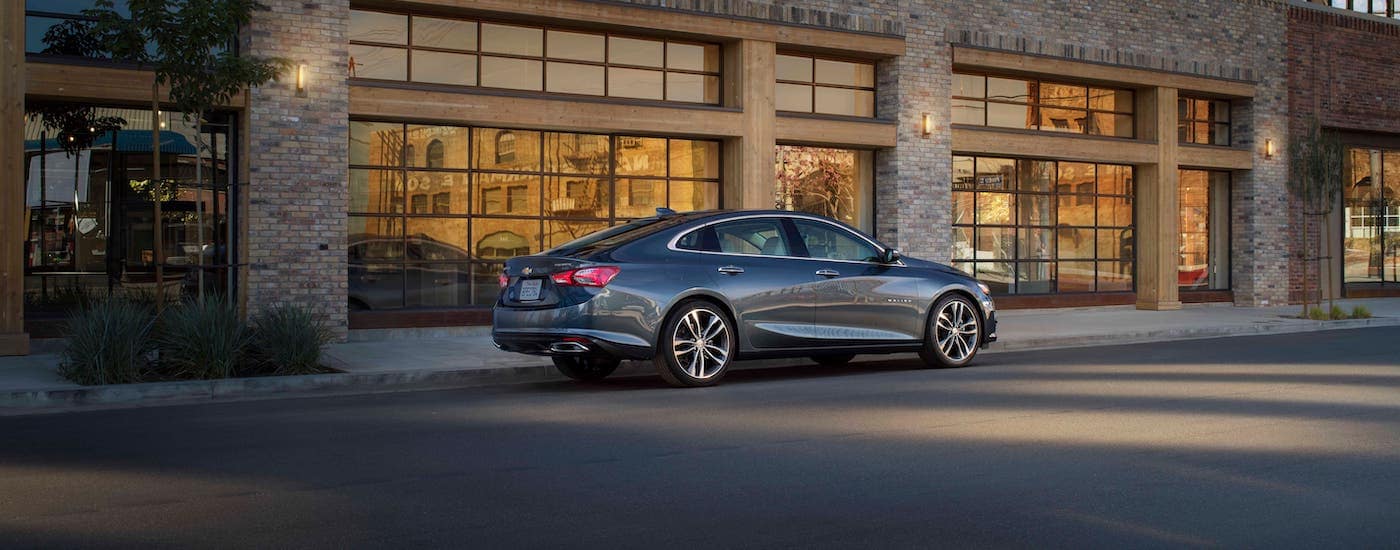 A gray 2020 Chevy Malibu is parked in front of a beige brick building.
