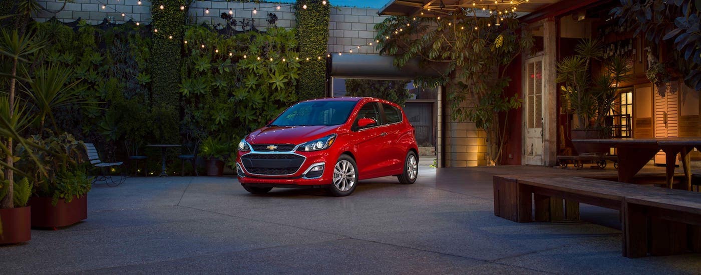 A red 2020 Chevy Spark, which is a popular model at a Chevy dealer near me, is parked in front of a restaurant near Suffolk, VA.