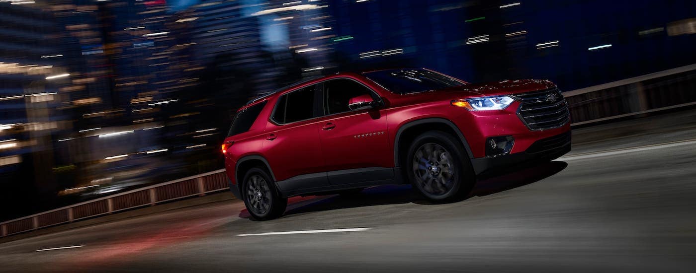 A red 2020 Chevy Traverse RS is driving on a city street at night.