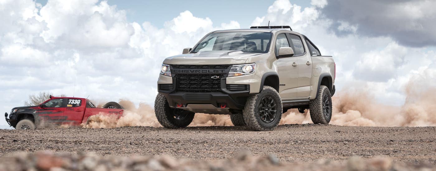 A red and a tab 2021 Chevy Colorado ZR2 are diving on a dirt track.