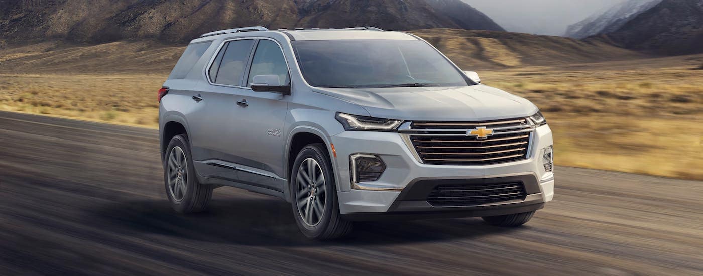 A silver 2022 Chevy Traverse is driving in a field with mountains in the distance.