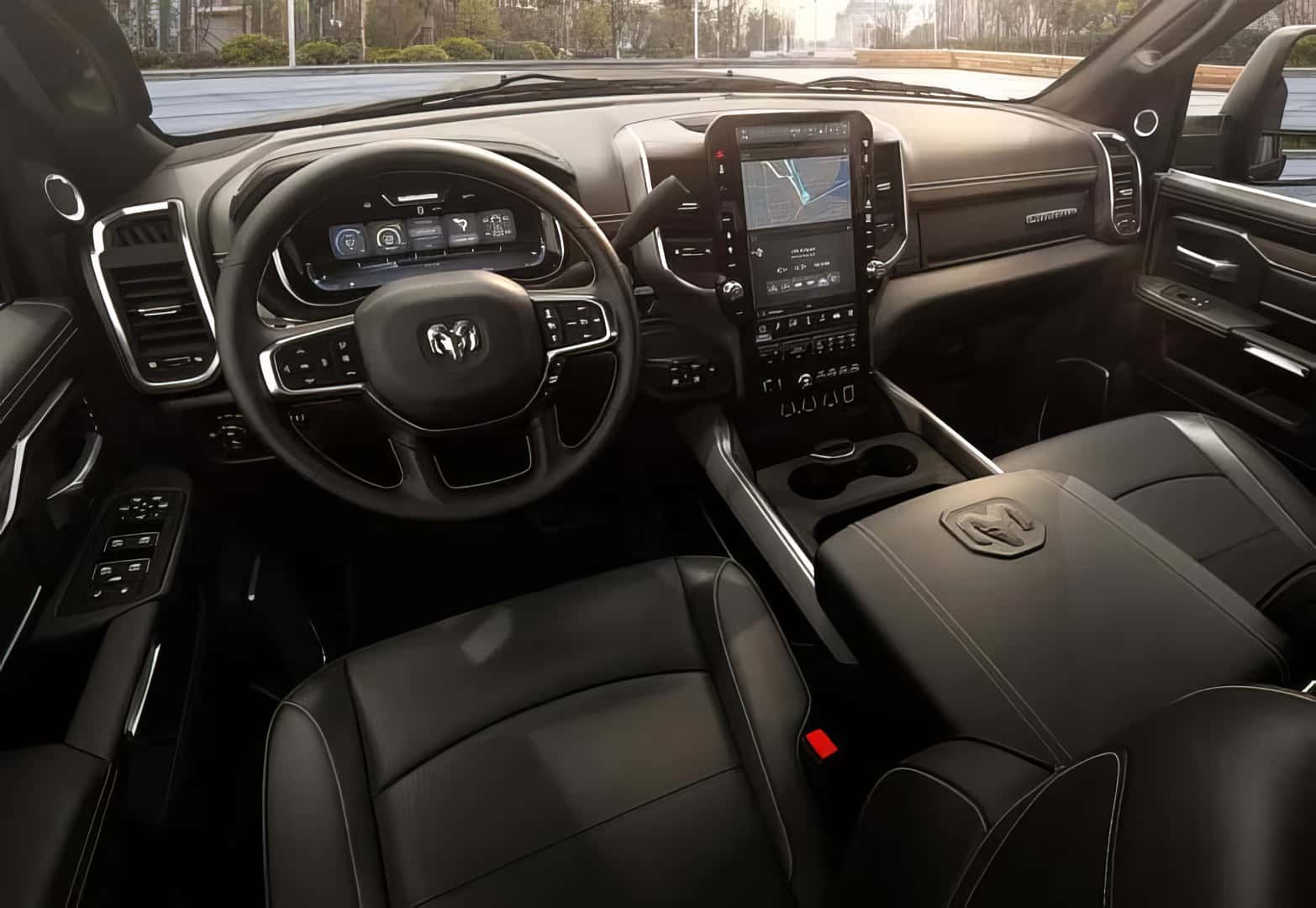 The interior of a Ram pickup truck is shown from the front passenger seat. The steering wheel is on the left, with a digital dashboard behind it. The center console features a large vertical touchscreen display showing a map. The seats and armrest are covered in black leather.