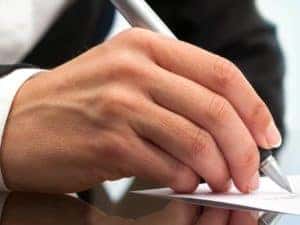 a man's hand signing paperwork on glass table