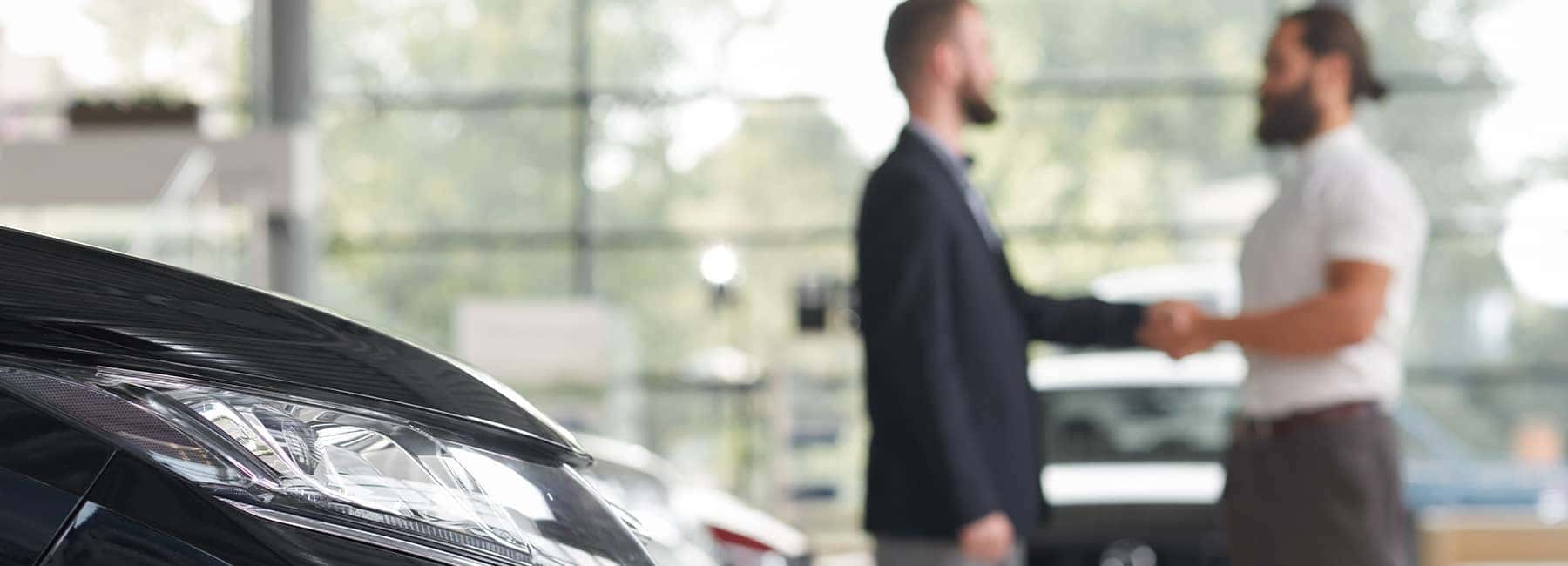 A car salesman and customer shake hands after agreeing on a purchase price