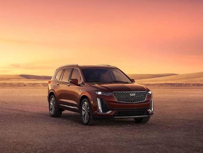 Cadillac XT6 parked out in the middle of the desert with the sun setting in the background