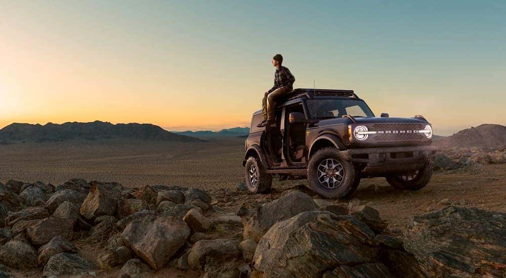 A black A red 2021 Ford Bronco Badlands Edition is parked in the desert with a person sitting on the roof looking into the distance.