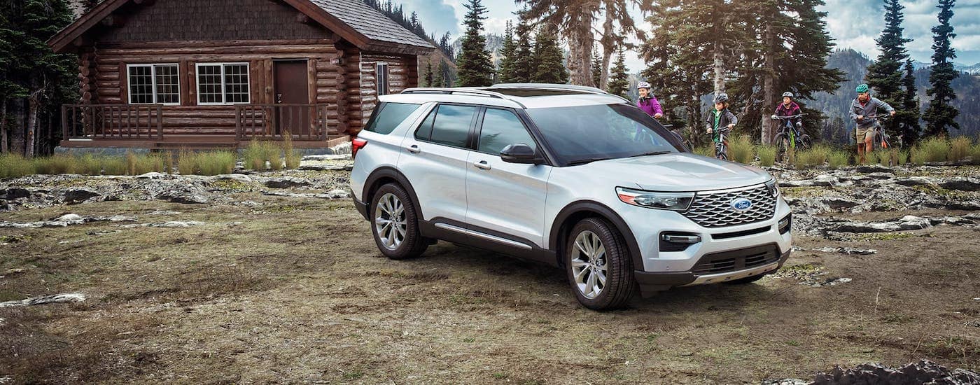 A white 2021 Ford Explorer is parked in front of a log cabin and a family on bikes.