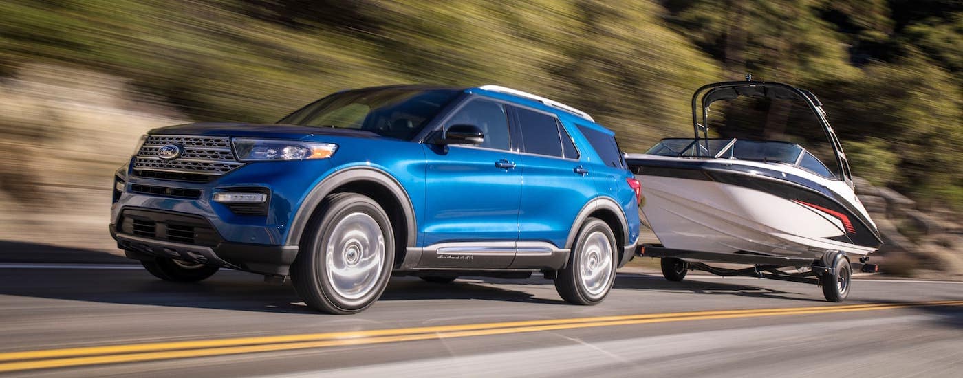 A blue 2021 Ford Explorer is towing a boat on a road past blurred trees.