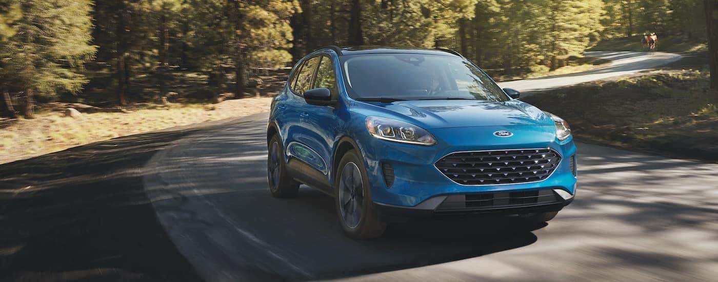 A blue 2021 Ford Escape is shown driving through a road in the woods."A blue 2021 Ford Escape is shown driving through a road in the woods.
