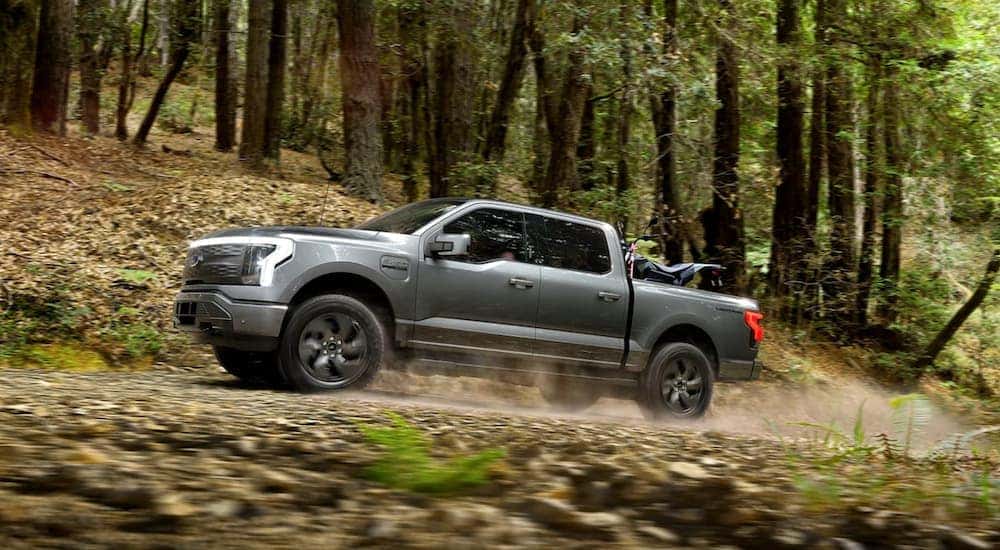 Side view of a silver 2022 Ford F-150 Lightning driving through the woods after leaving a Canon City car dealership.