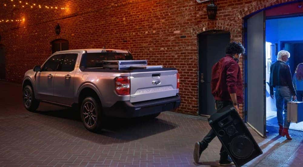A silver 2022 Ford Maverick is parked in front of a brick wall outside of a concert.