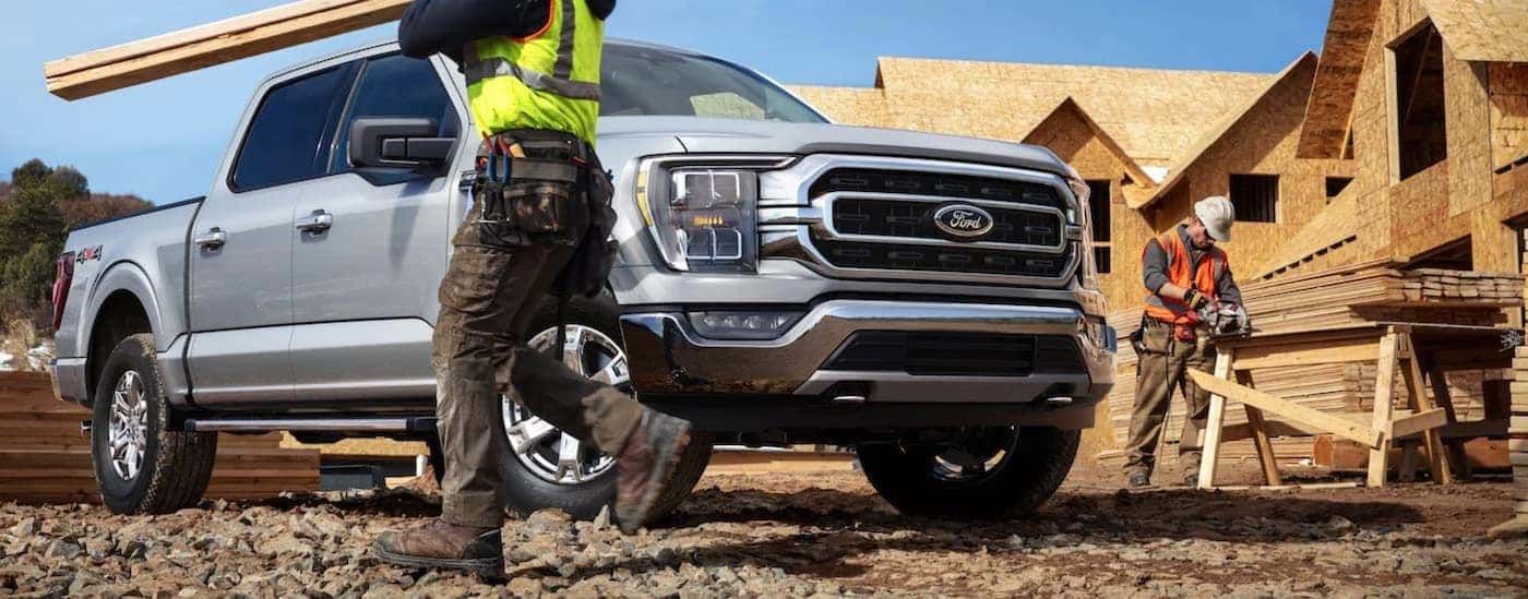 A silver 2021 Ford F-150 is parked at a construction site and surrounded by carpenters.