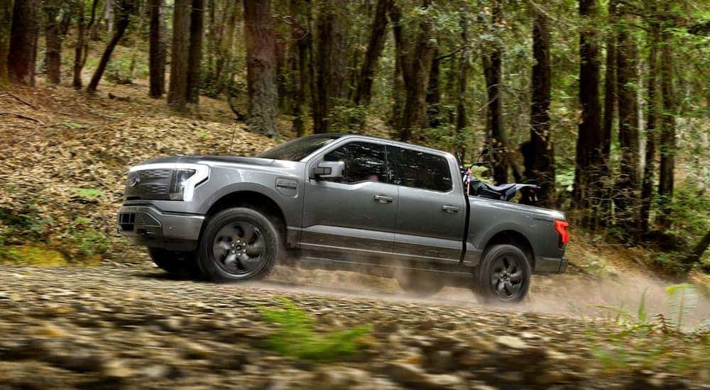 A grey 2022 Ford F-150 Lightning is shown from the side off-roading through the forest.