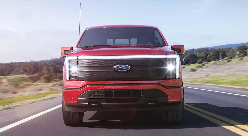 A red 2022 Ford F-150 Lightning is shown from the front driving on an open road after leaving a Ford Lightning dealer.