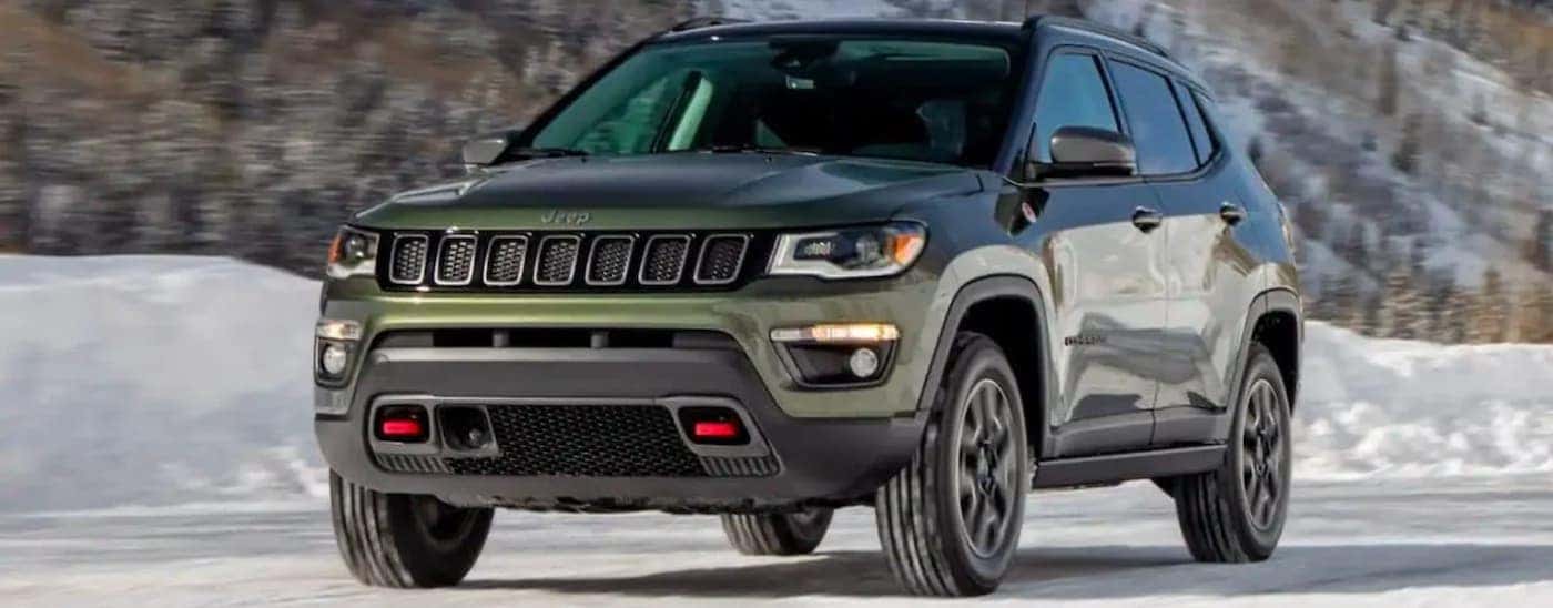 A green 2019 Jeep Compass Trailhawk is driving on a snowy road.