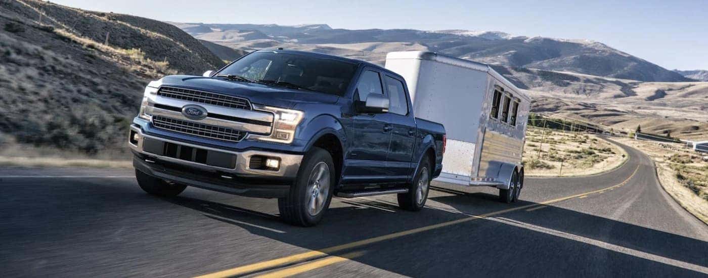 A blue 2019 Ford F-150 is towing an enclosed trailer on a highway.