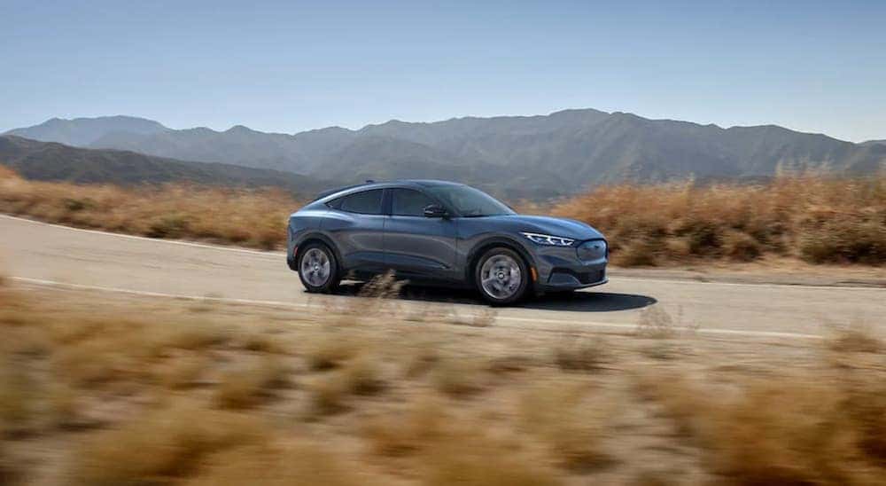 A grey 2021 Ford Mustang Mach-E driving on a rural road with mountains in the distance.