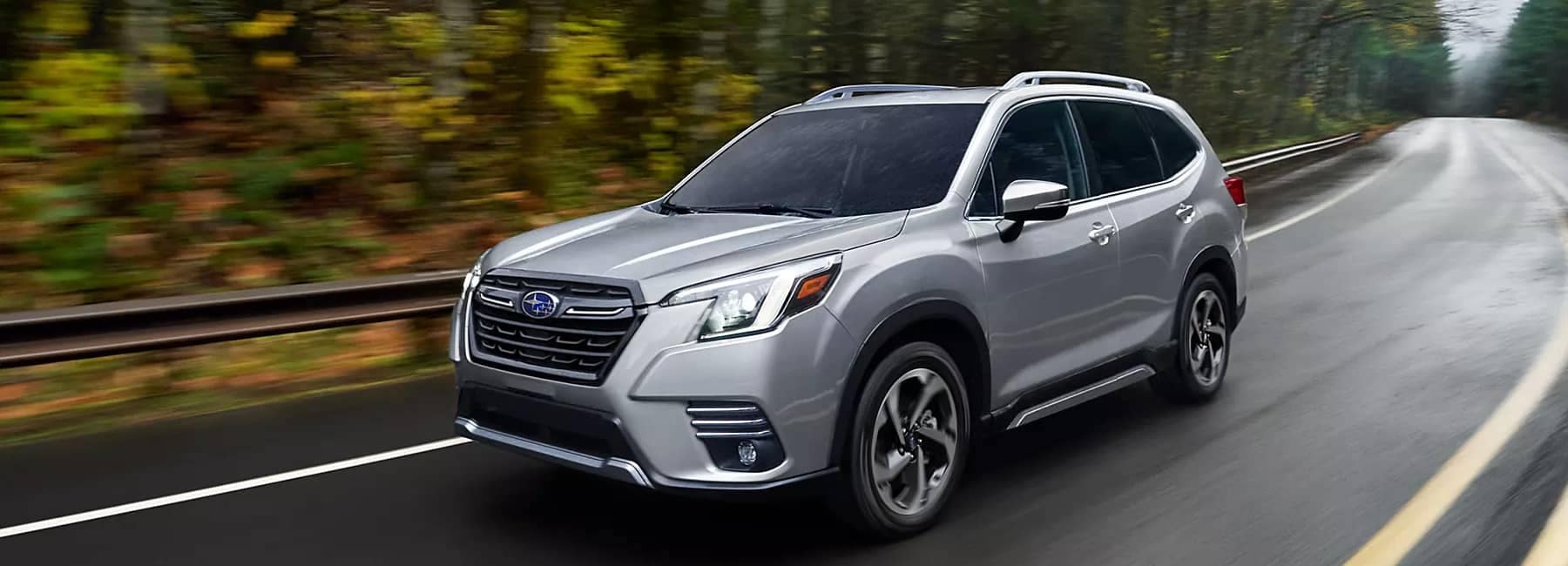 2022 Subaru Forester- front-3qview driving highway- blurred forest background-silver