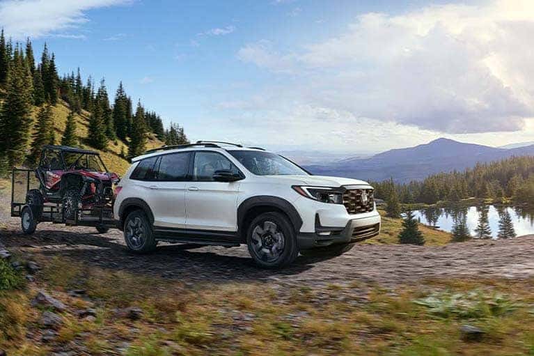 A-white-2022-Honda-Passport-pulling-an-ATV-by-a-mountain-lake