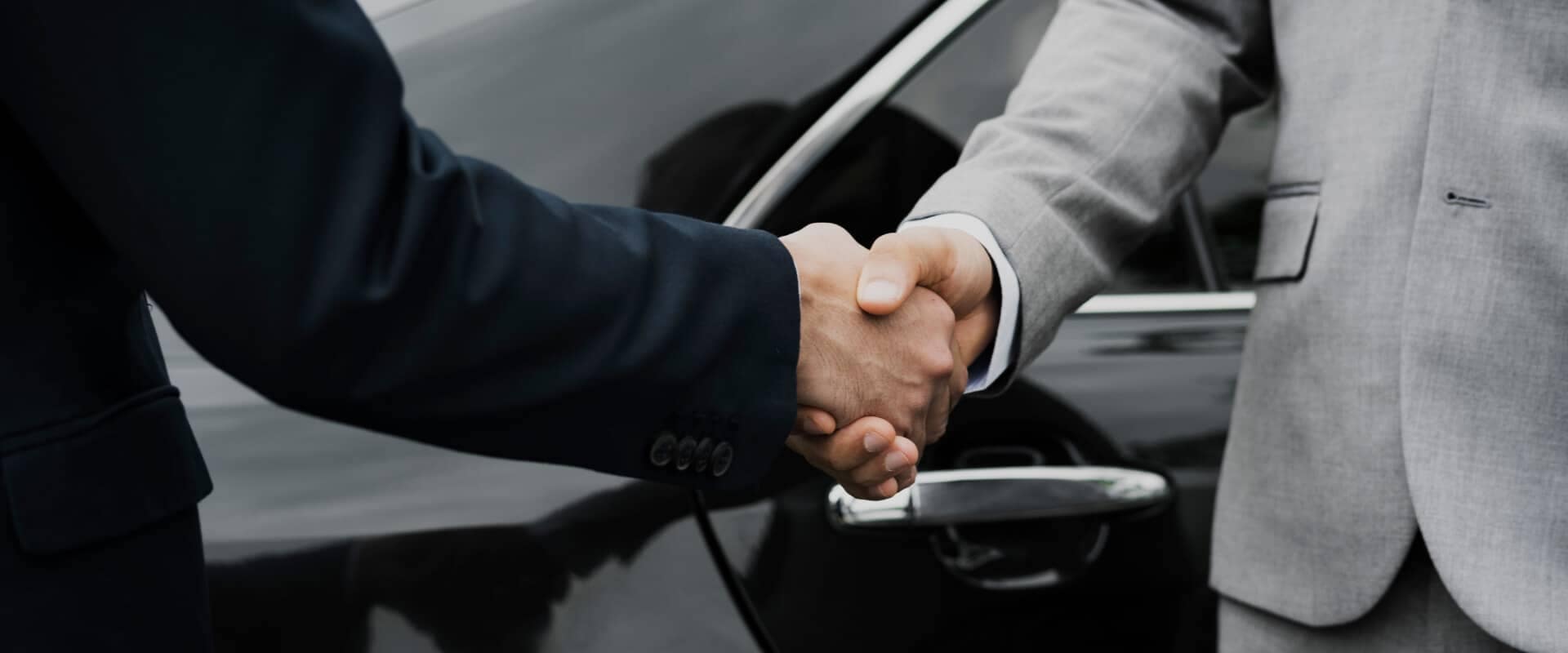 Two people shaking hands with a Mazda car in the background