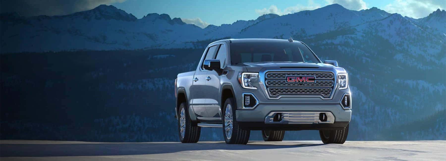 A silver GMC truck parked in front of a mountain range.