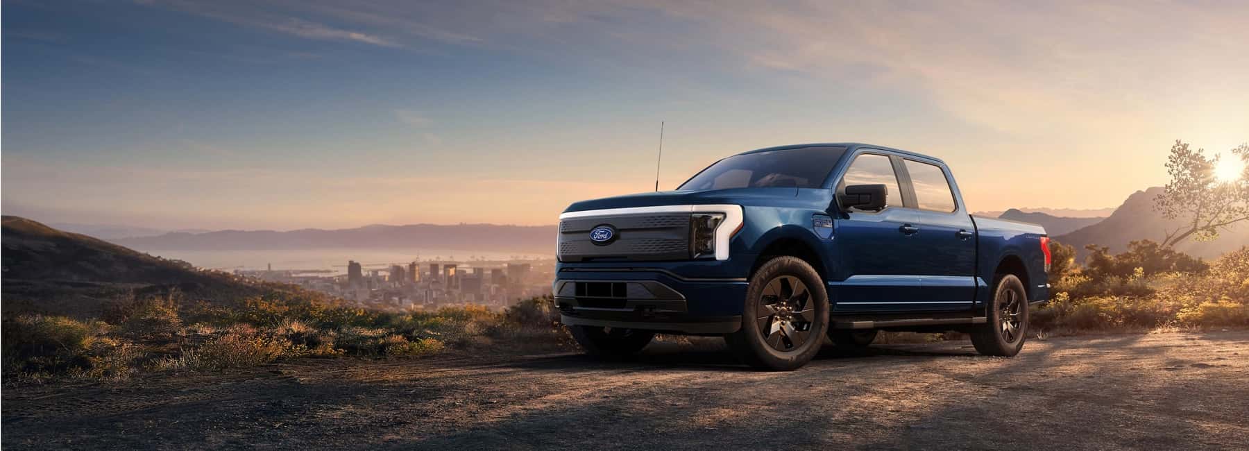 2025-Ford-F-150-Lightning-parked-on-gravel-lot-with-city-scape-in-a-valley-in-background