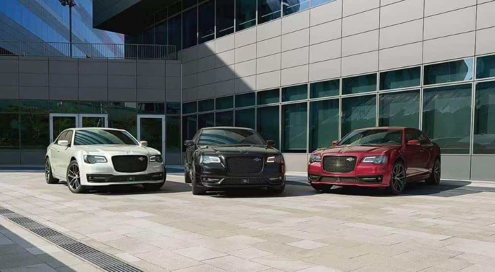 A white, a black, and a red 2022 Chrysler 300C are shown in front of a modern building.