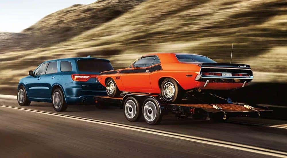 A blue 2024 Dodge Durango is shown towing an orange 1970 Dodge Challenger.
