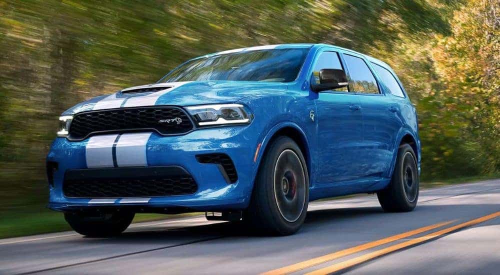 A blue 2024 Dodge Durango SRT is shown driving on a tree-lined road after leaving a Dodge dealer.