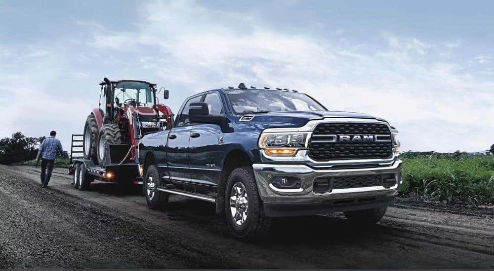 A blue 2024 Ram 2500 is shown towing a tractor after leaving a Ram dealer.