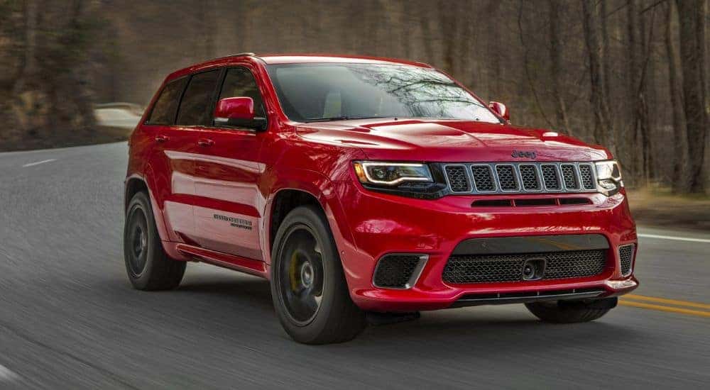 A red 2018 Jeep Grand Cherokee Trackhawk is shown on a tree-lined road after leaving a used Jeep dealership.