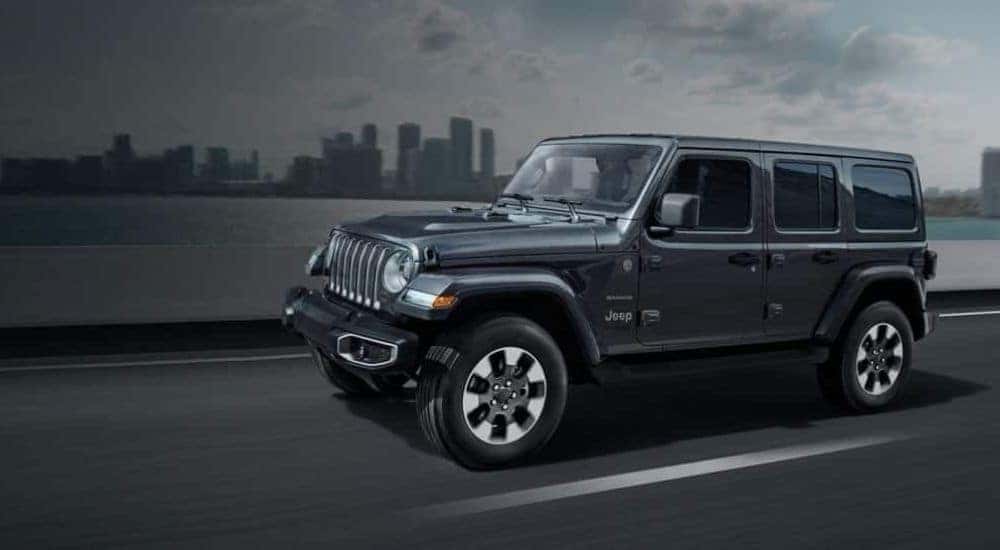A grey 2018 Jeep Wrangler Sahara Unlimited is shown driving past a city.