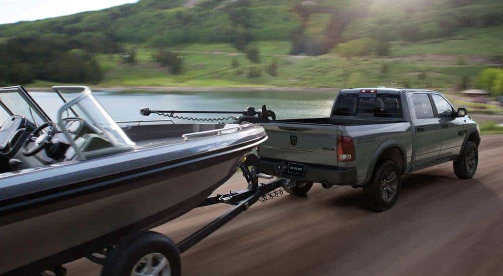 A grey 2023 Ram 1500 Warlock is shown towing a boat past a lake.