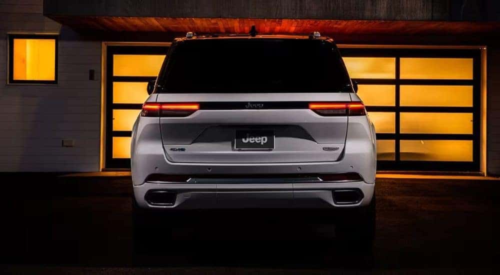 A white 2023 Jeep Grand Cherokee 4xe is shown from the rear parked near a garage.