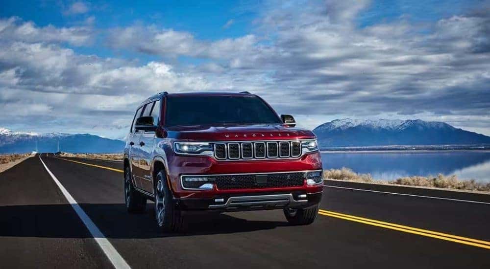 A red 2024 Jeep Wagoneer is shown driving past a lake after leaving a Jeep dealer near Mount Holly.